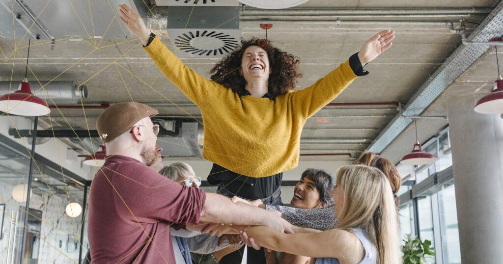 Eine Frau wirft sich lachend und mit ausgestreckten Armen in die Arme ihrer Kollegen, die sie sicher auffangen