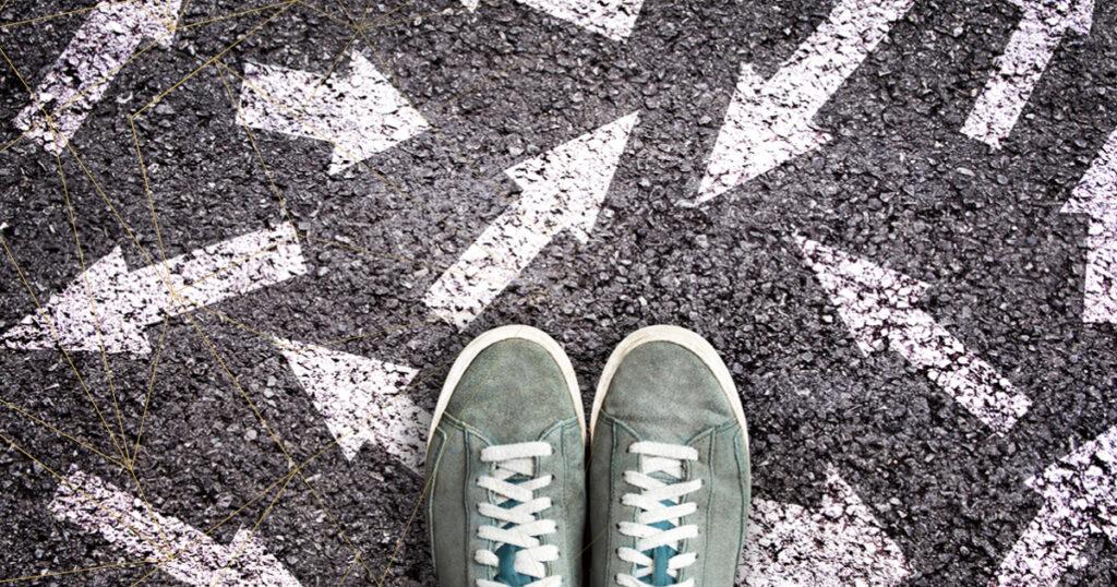 Ein Paar grüne Sneakers steht auf einer asphaltierten Fläche, auf der weiße Pfeile in verschiedene Richtungen zeigen.