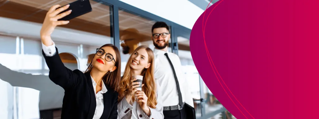 Zwei Frauen und ein Mann in Business-Outfit machen ein Selfie von sich im B&uuml;ro