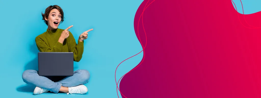 Eine Frau sitzt im Schneidersitz vor einem blauen Hintergrund. Sie zeigt mit beiden Zeigefingern nach oben rechts und schaut dabei &uuml;berrascht.