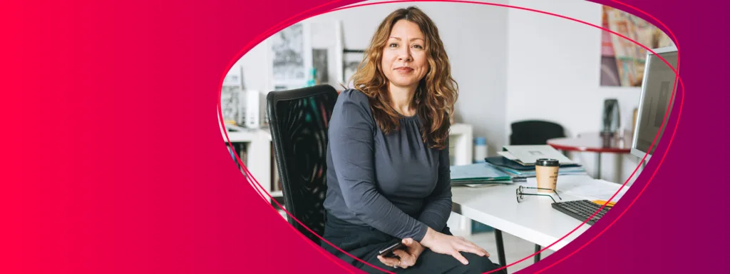 Frau sitzt an einem Schreibtisch im Büro und blickt in die Kamera