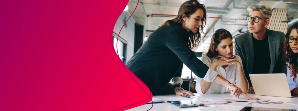 Vier Menschen besprechen an einem Tisch Unterlagen und schauen auf einen Laptop.