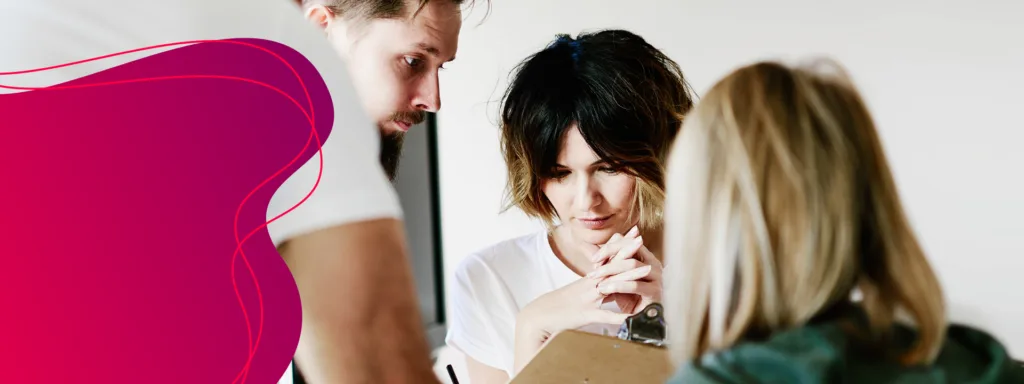 Zwei Frauen und ein Mann schauen im Arbeitskontext auf ein Klemmbrett